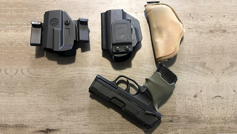 Assortment of holsters, including one large, one medium, and one small, placed with a handgun
