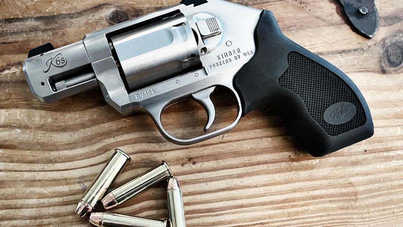 A revolver rests on a wooden table, with a bullet placed on top